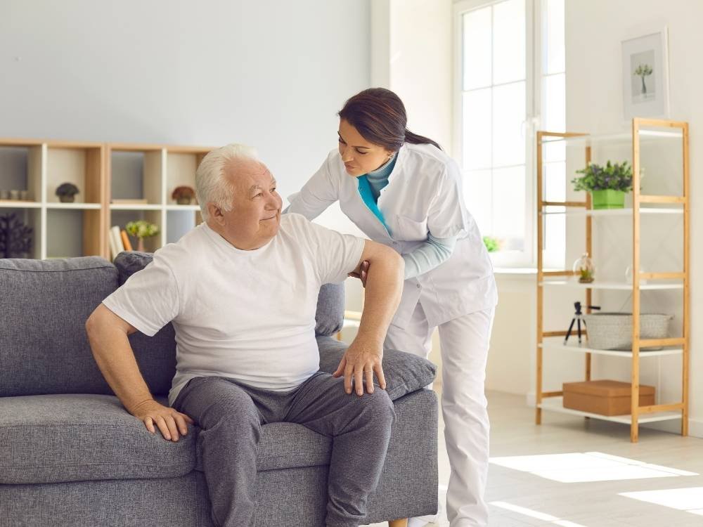 Illustrative caregiver assisting an older woman with movement at home